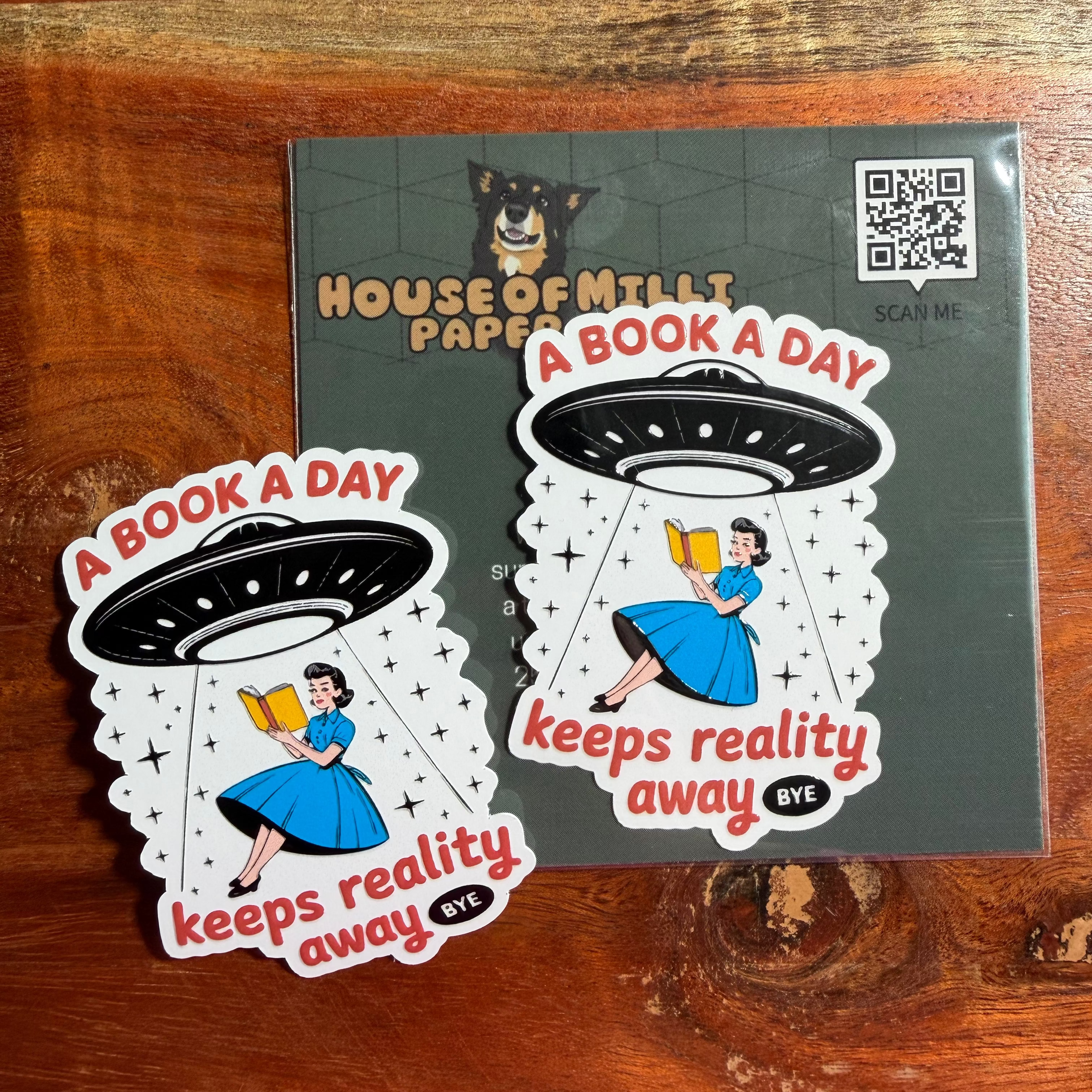 Two 'A Book A Day' stickers with a woman reading a book in a UFO design on a House of Milli Paper card.