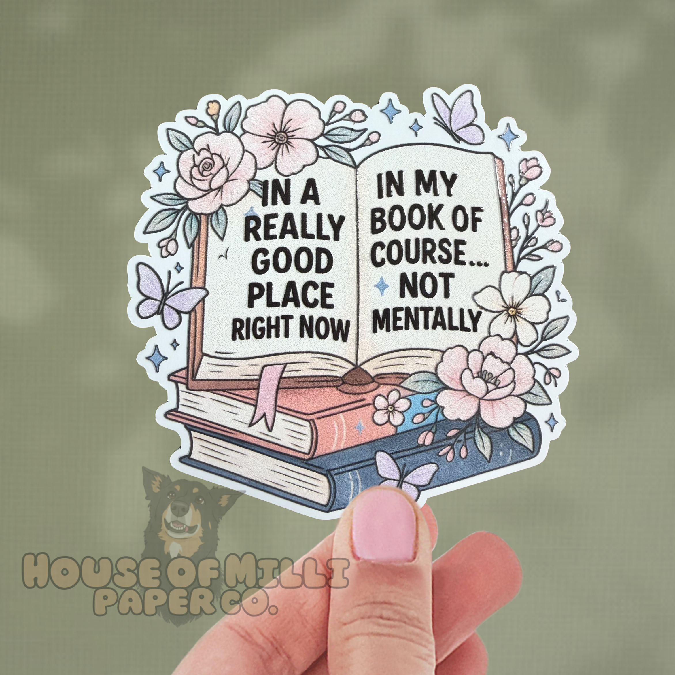 Sticker of an open book with floral elements held by a hand, with 'House of Milly Paper Co.' branding.