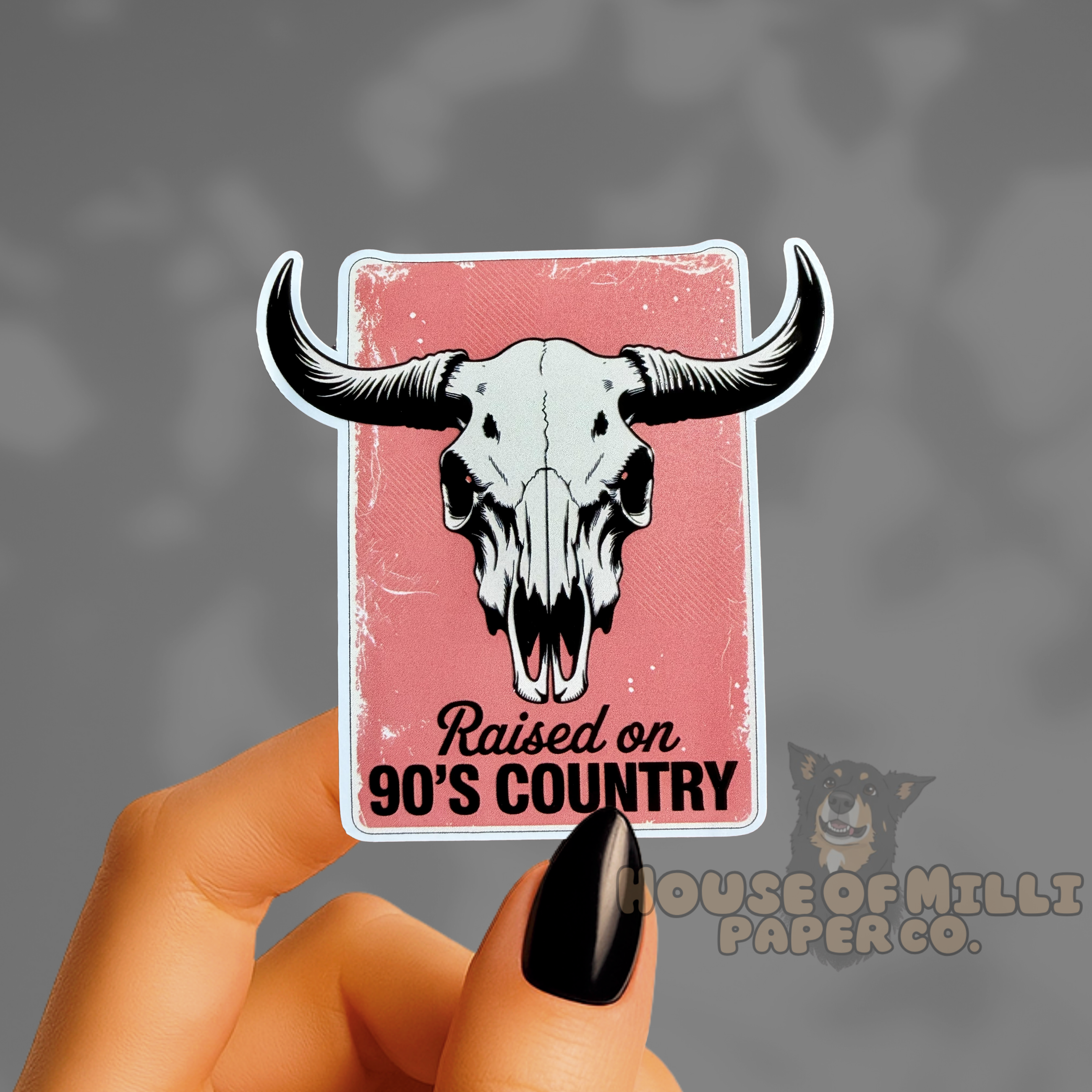 Sticker with bull skull design and text 'Raised on 90's Country' held by a hand.