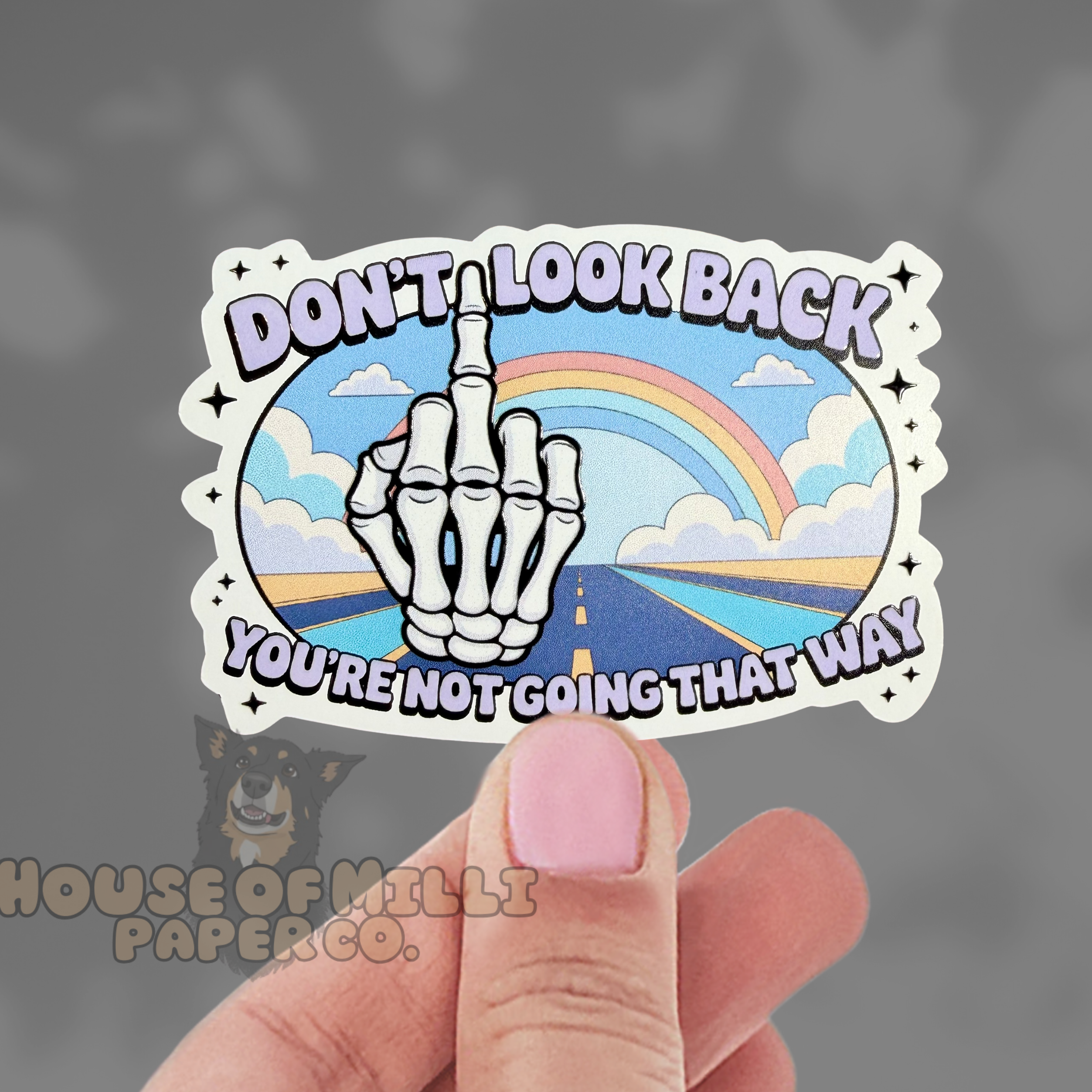 Sticker with skeleton hand and rainbow design held by a hand against a dark background