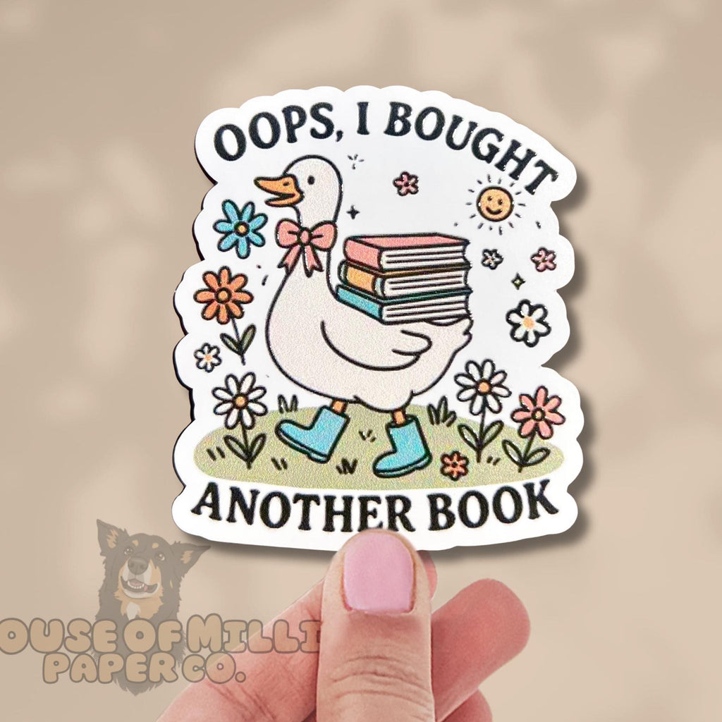 Sticker with a duck holding books and text 'Oops, I bought another book' held by a hand.