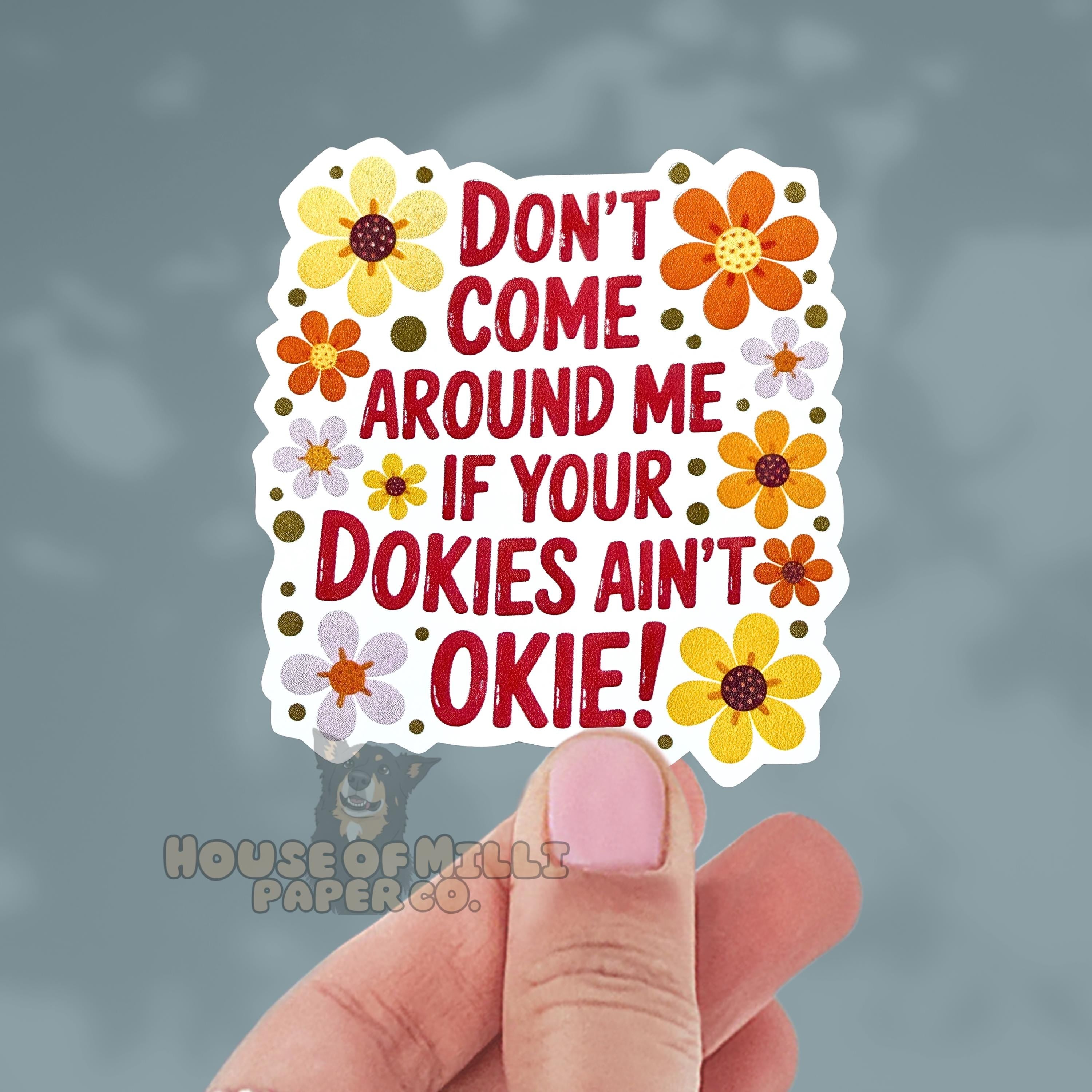 Hand holding a colorful sticker with text and flowers on a gray background