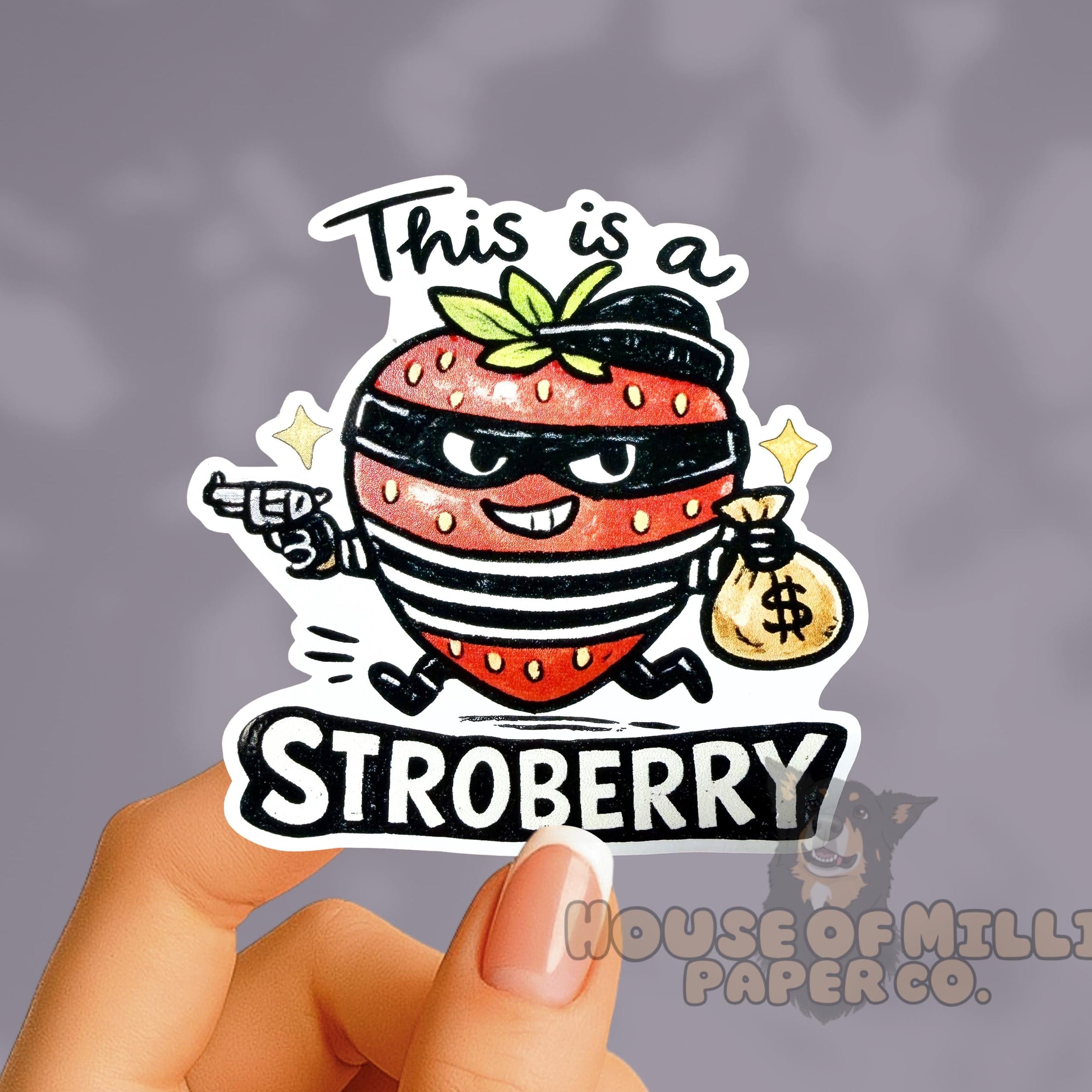 Sticker of a strawberry character holding a bag with money and text 'This is a STROBBERRY' held by a hand against a dark background.
