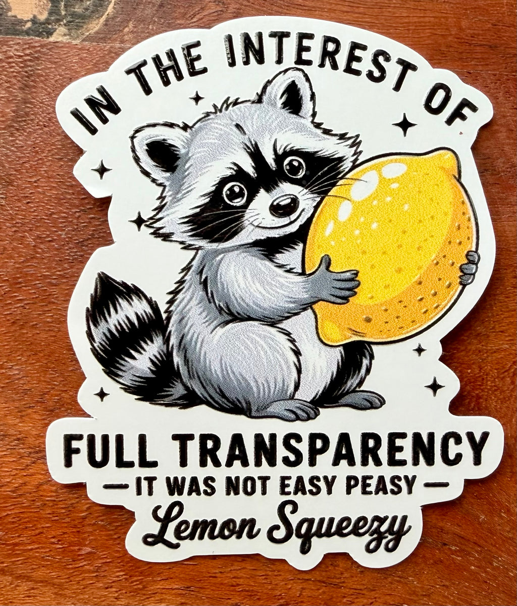 Sticker with a raccoon holding a lemon and humorous text on a wooden surface