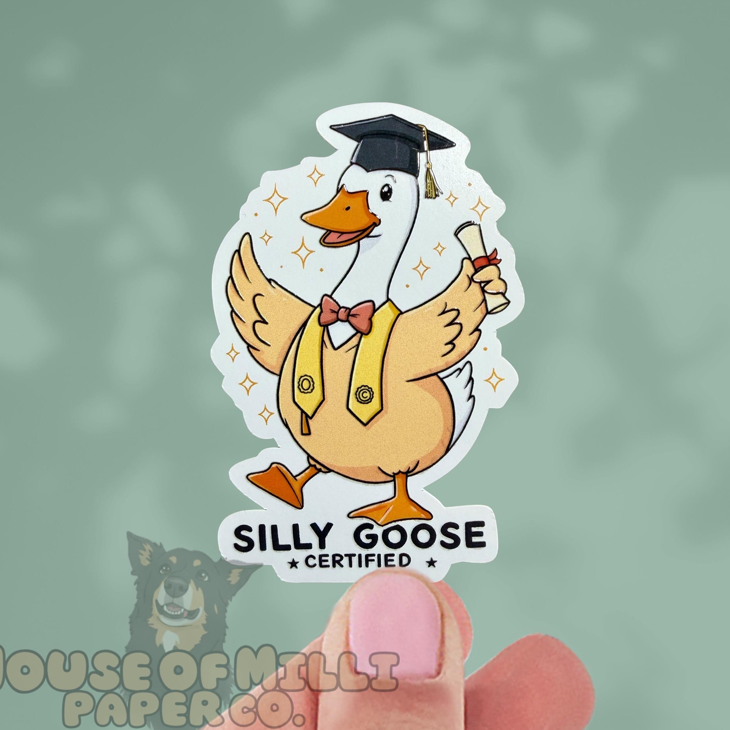 Sticker of a cartoon goose in a graduation outfit held by a hand with a blurred background.