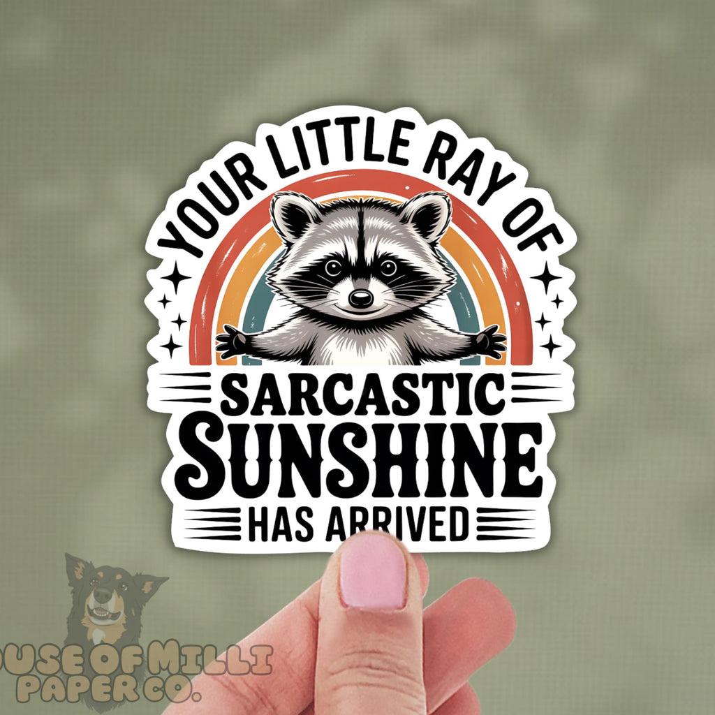 Sticker with raccoon illustration and text held by a hand on a green background