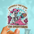 Sticker with skeleton pouring pink powder, text 'I sprinkle this stuff on everything', and cacti on a light blue background.
