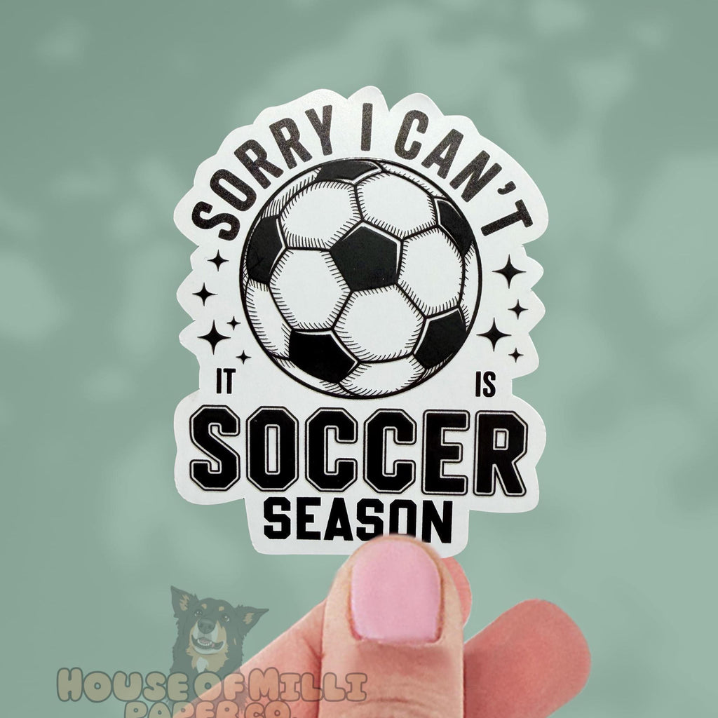 Sticker with soccer ball and text 'Sorry I can't it is soccer season' held by a hand against a green background.