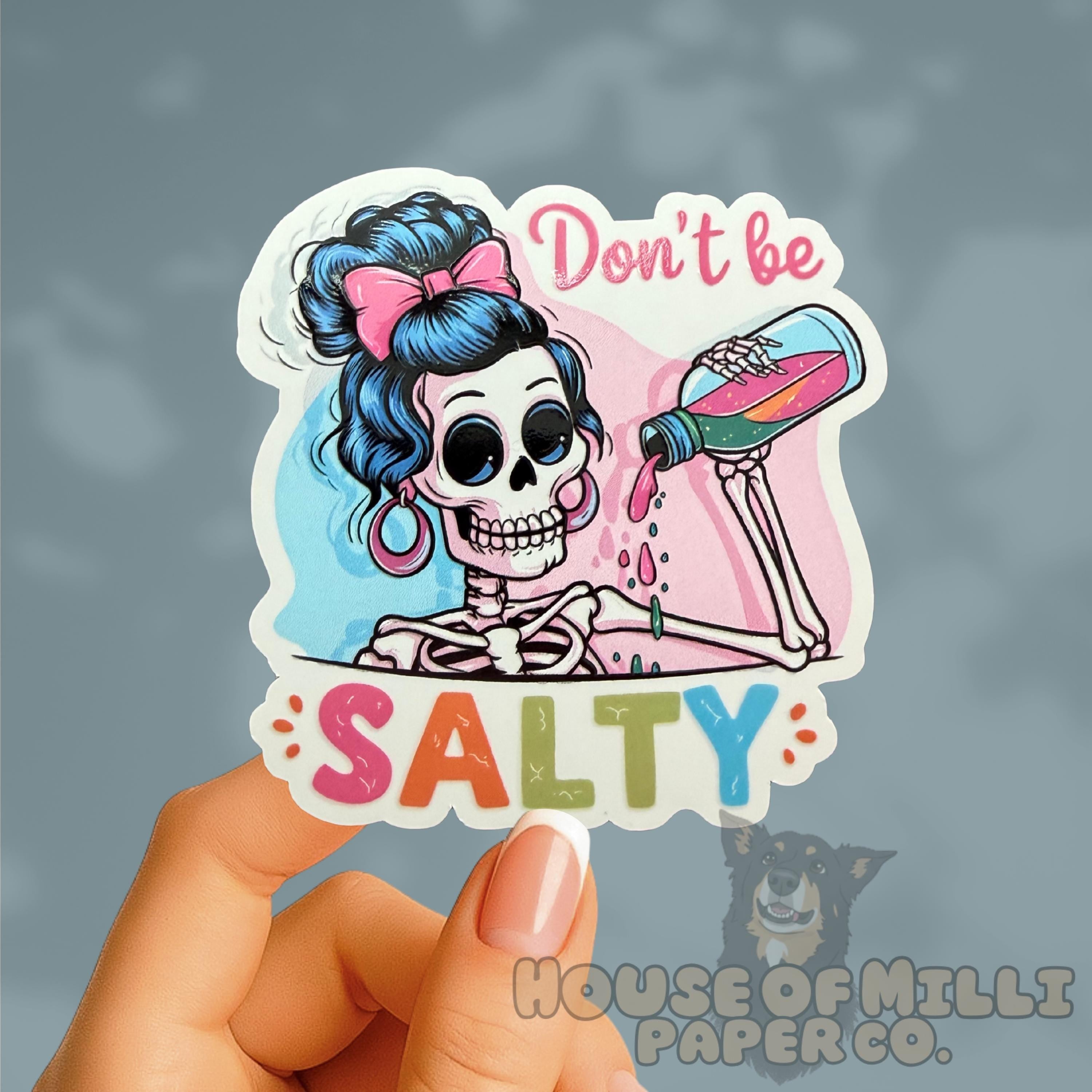 Sticker with a skeleton character and text 'Don't be Salty' held by a hand against a gray background.