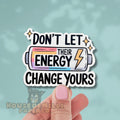Sticker with motivational text 'Don't let their energy change yours' held by a hand on a light blue background.